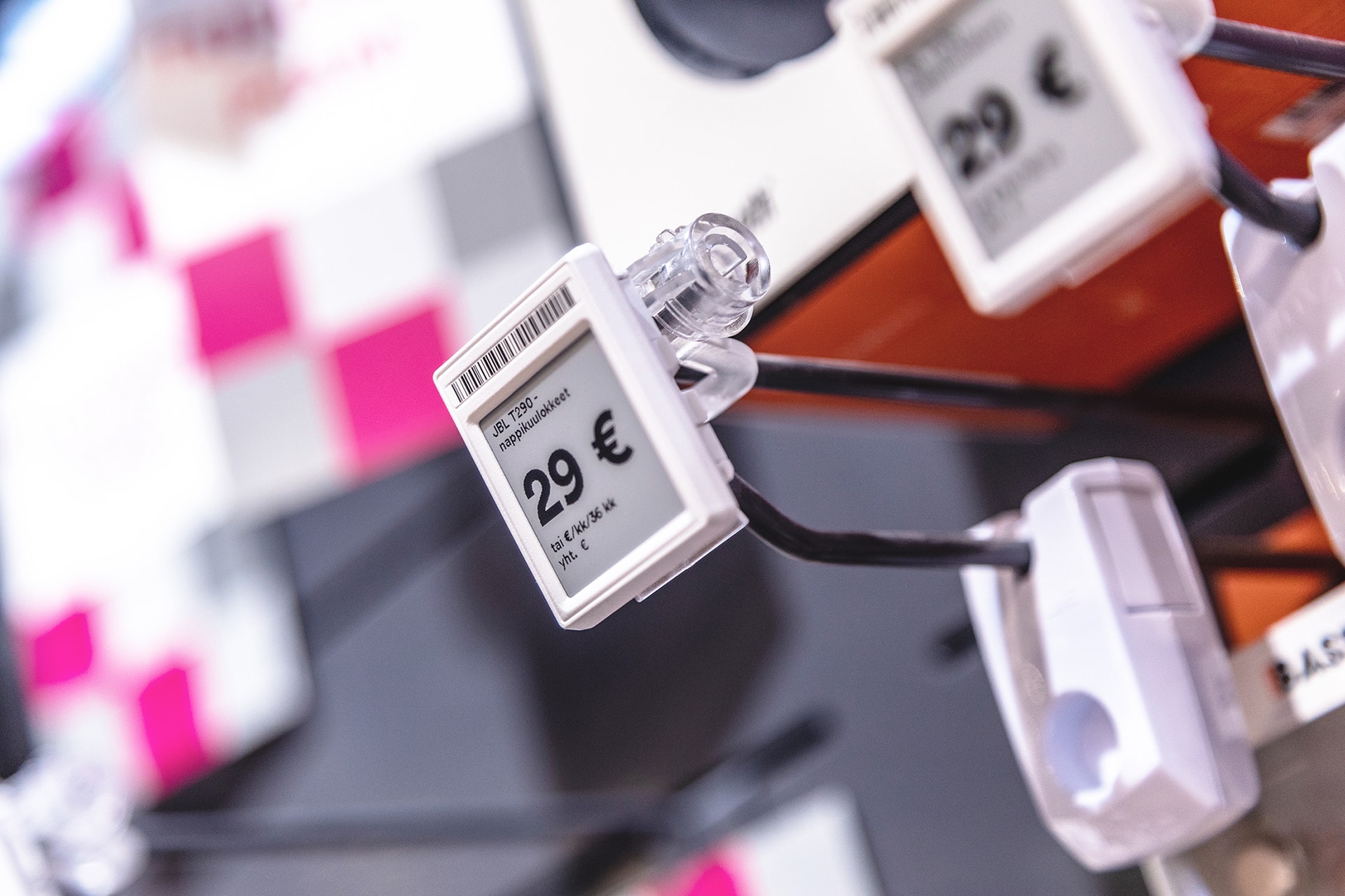 Close-up of a white electronic price tag showing 29 € with a barcode on a display peg, background blurred