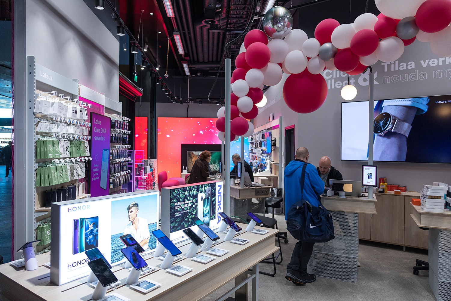 Interior of a tech store with phone displays, product stands, and pink/white balloons overhead